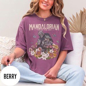 Puede incluir: Camiseta color bayas con un gr&aacute;fico del Mandaloriano y Grogu rodeados de flores y mariposas. El texto "MANDALORIAN - THIS IS THE WAY" est&aacute; impreso en la parte superior. La camiseta tiene mangas cortas y un corte holgado.