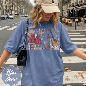 May include: A blue t-shirt featuring a graphic print of a cowboy hat, a red paisley cardigan, a sheriff badge labeled Sheriff Taylor, a microphone, a cowboy boot, an acoustic guitar, and blocks spelling Toy Story with a black shoulder bag.