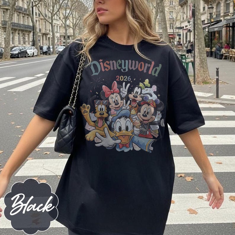 Pu&ograve; includere: T-shirt nero con una grafica colorata di personaggi Disney, tra cui Topolino, Minnie e Paperino. Il testo "Disneyworld 2026" &egrave; stampato sopra i personaggi. La maglietta &egrave; in stile casual.