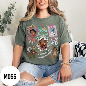 Pu&ograve; includere: T-shirt verde muschio con un design grafico colorato con personaggi ed elementi di un popolare film d'animazione. Il design include ritratti incorniciati, fiocchi e altri elementi decorativi. La parola "MOSS" &egrave; stampata su un cerchio bianco.