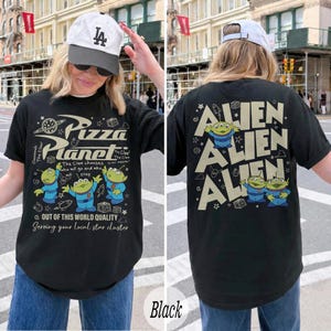 K&ouml;nnte beinhalten: Schwarzes T-Shirt mit Pizza Planet-Logo und Alien-Charakteren. Auf der Vorderseite befindet sich das Pizza Planet-Logo und Text. Auf der R&uuml;ckseite steht das Wort "Alien" wiederholt. Das T-Shirt hat eine bequeme Passform.