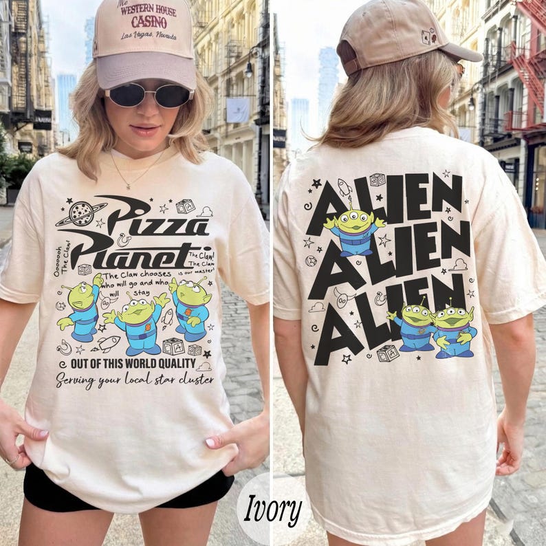K&ouml;nnte beinhalten: Elfenbeinfarbenes Pizza Planet T-Shirt mit einer Grafik von drei gr&uuml;nen Aliens und dem Pizza Planet Logo auf der Vorderseite. Auf der R&uuml;ckseite des Shirts steht das Wort "ALIEN" wiederholt mit Alien-Grafiken.