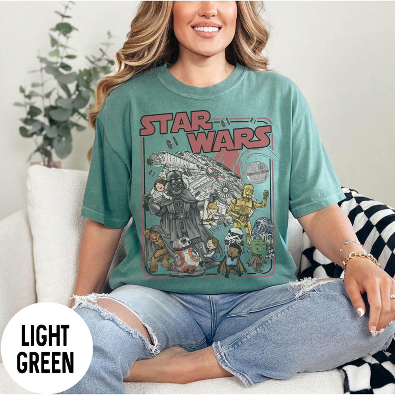 May include: Light green Star Wars graphic t-shirt featuring Darth Vader, the Millennium Falcon, and other characters. The shirt has the words "Star Wars" in red and white. The shirt is made of a soft material.
