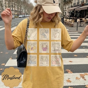 May include: Mustard-colored t-shirt featuring a grid of cartoon illustrations with dates. The illustrations are in a line-drawing style. The word "Mustard" is written in a cursive font at the bottom left of the shirt.