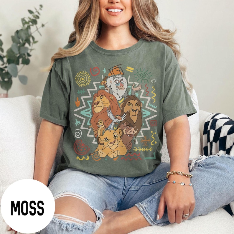 Puede incluir: Camiseta verde musgo con un gr&aacute;fico colorido de personajes de El Rey Le&oacute;n. El dise&ntilde;o incluye a Simba, Mufasa, Scar, Tim&oacute;n, Pumba y Zaz&uacute;, con patrones de inspiraci&oacute;n tribal. La camiseta es de corte holgado.