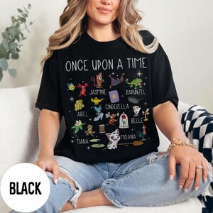 May include: Black t-shirt with the words "ONCE UPON A TIME" and cartoon character illustrations. The shirt features characters like Ariel, Jasmine, Cinderella, and Belle. The word "BLACK" is printed on a white circle.