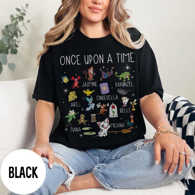 May include: Black t-shirt with the words "ONCE UPON A TIME" and cartoon character illustrations. The shirt features characters like Ariel, Jasmine, Cinderella, and Belle. The word "BLACK" is printed on a white circle.