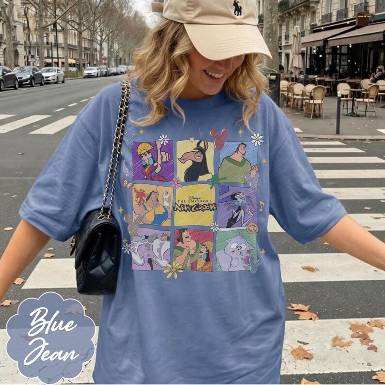 May include: A blue jean colored t-shirt featuring a grid of nine panels displaying characters from the movie The Emperor's New Groove, including Kuzco, Pacha, and Yzma, with small flower and musical note accents printed on the front of the garment.