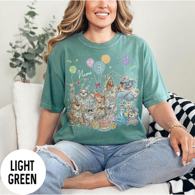 以下が含まれることがあります： 誕生日を祝う動物たちが描かれた、カラフルな漫画デザインのライトグリーンのTシャツ。デザインには風船、ケーキ、数字の3が含まれています。「Name」の文字も表示されています。