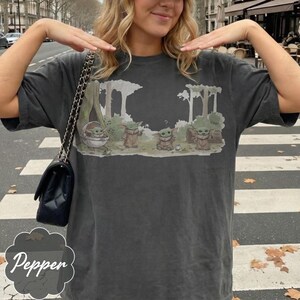 Puede incluir: Camiseta gris oscuro con un gr&aacute;fico de Grogu de The Mandalorian. El dise&ntilde;o muestra a Grogu en una c&aacute;psula y de pie con otros personajes en un entorno forestal. La palabra "cool" tambi&eacute;n est&aacute; en el dise&ntilde;o.