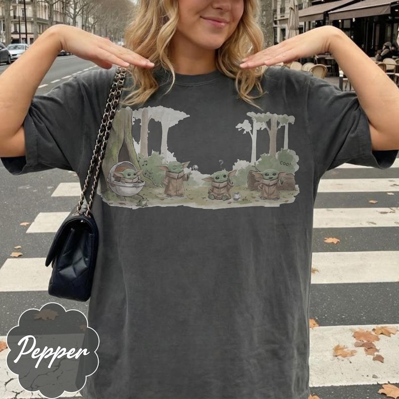 Puede incluir: Camiseta gris oscuro con un gr&aacute;fico de Grogu de The Mandalorian. El dise&ntilde;o muestra a Grogu en una c&aacute;psula y de pie con otros personajes en un entorno forestal. La palabra "cool" tambi&eacute;n est&aacute; en el dise&ntilde;o.
