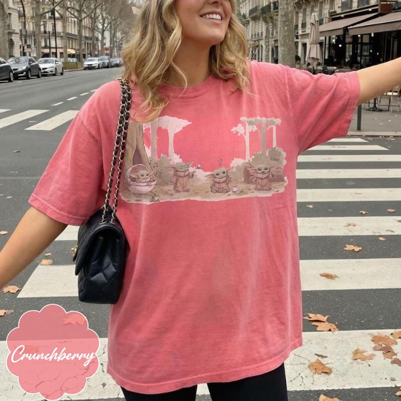 Puede incluir: Una camiseta de color coral con un gr&aacute;fico de Grogu de The Mandalorian. El dise&ntilde;o muestra a Grogu en una c&aacute;psula y con otros personajes en un entorno forestal. La camiseta tiene mangas cortas y un corte holgado.