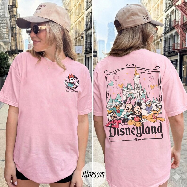 Pu&ograve; includere: T-shirt rosa chiaro con un motivo di Minnie Mouse sul davanti e una grafica di Disneyland sul retro. La grafica di Disneyland include personaggi dei cartoni animati e un castello. La maglietta ha maniche corte e scollo tondo.