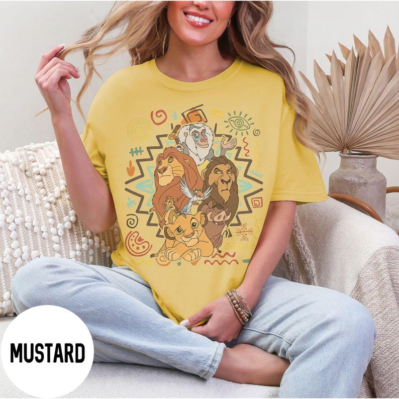 Puede incluir: Camiseta de color mostaza con un gr&aacute;fico de personajes de El Rey Le&oacute;n. El dise&ntilde;o incluye a Simba, Mufasa, Scar, Tim&oacute;n, Pumba y Rafiki, con patrones de inspiraci&oacute;n tribal. La palabra "MUSTARD" est&aacute; impresa en la parte inferior izquierda.
