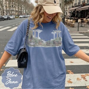 Puede incluir: Camiseta azul vaquero con un gr&aacute;fico de Grogu de The Mandalorian. El dise&ntilde;o incluye a Grogu en varias poses en un entorno forestal. La camiseta tiene mangas cortas y un corte holgado. Las palabras "Blue Jean" est&aacute;n escritas en cursiva.