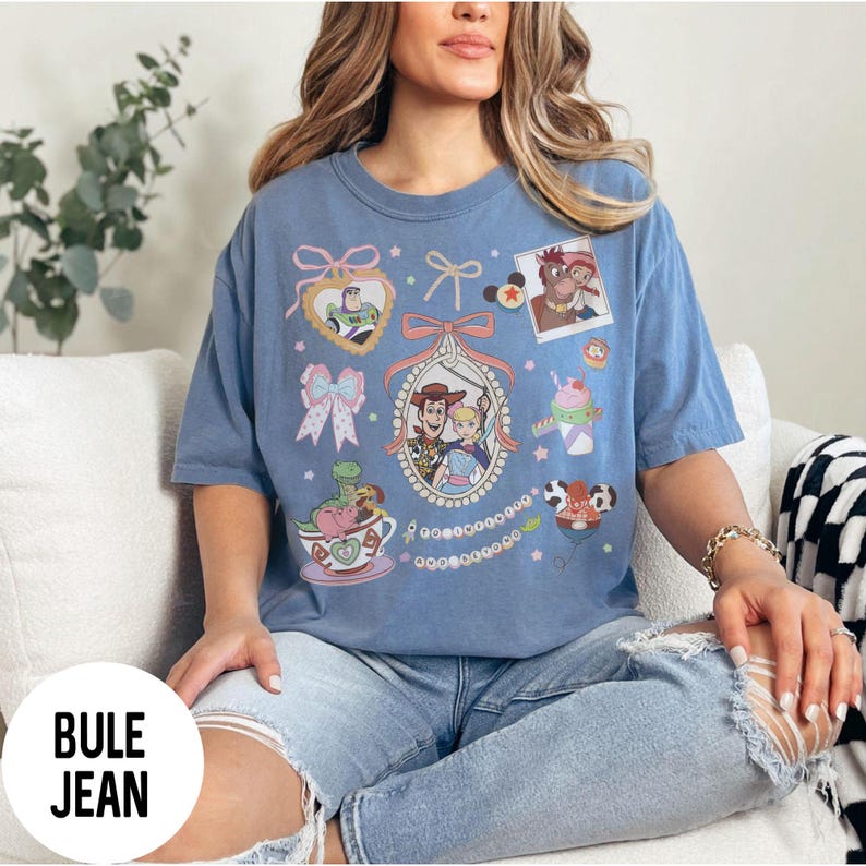 May include: Blue t-shirt featuring a colorful graphic of Toy Story characters. The design includes Buzz Lightyear, Woody, Bo Peep, and other elements. The shirt has a round neck and short sleeves.