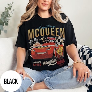 Op de afbeelding: Zwart T-shirt met een afbeelding van Lightning McQueen uit de film Cars. Het ontwerp bevat de gouden tekst "Lightning McQueen", een rode raceauto en de zinnen "Ultimate Speed" en "Think Fast."