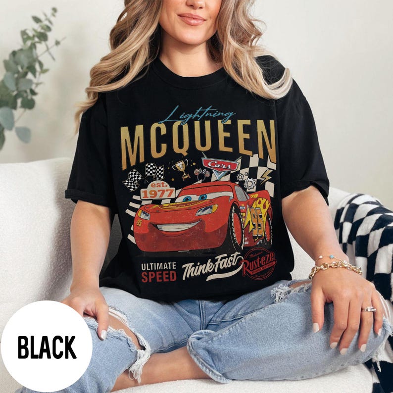 Op de afbeelding: Zwart T-shirt met een afbeelding van Lightning McQueen uit de film Cars. Het ontwerp bevat de gouden tekst "Lightning McQueen", een rode raceauto en de zinnen "Ultimate Speed" en "Think Fast."
