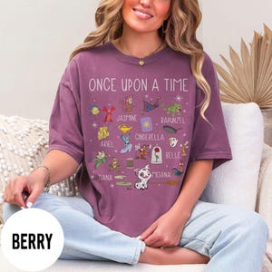 May include: Berry-coloured t-shirt with the text "ONCE UPON A TIME" and various cartoon character illustrations. The shirt features characters like Ariel, Jasmine, Cinderella, and Belle. The word "BERRY" is printed on a white circle.