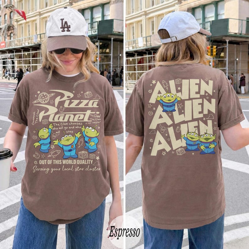 K&ouml;nnte beinhalten: Espressofarbenes T-Shirt mit dem Pizza Planet-Logo und Alien-Charakteren. Auf der Vorderseite des Shirts steht "Pizza Planet" und "Out of this world quality". Auf der R&uuml;ckseite des Shirts steht "Alien" und Alien-Charaktere.