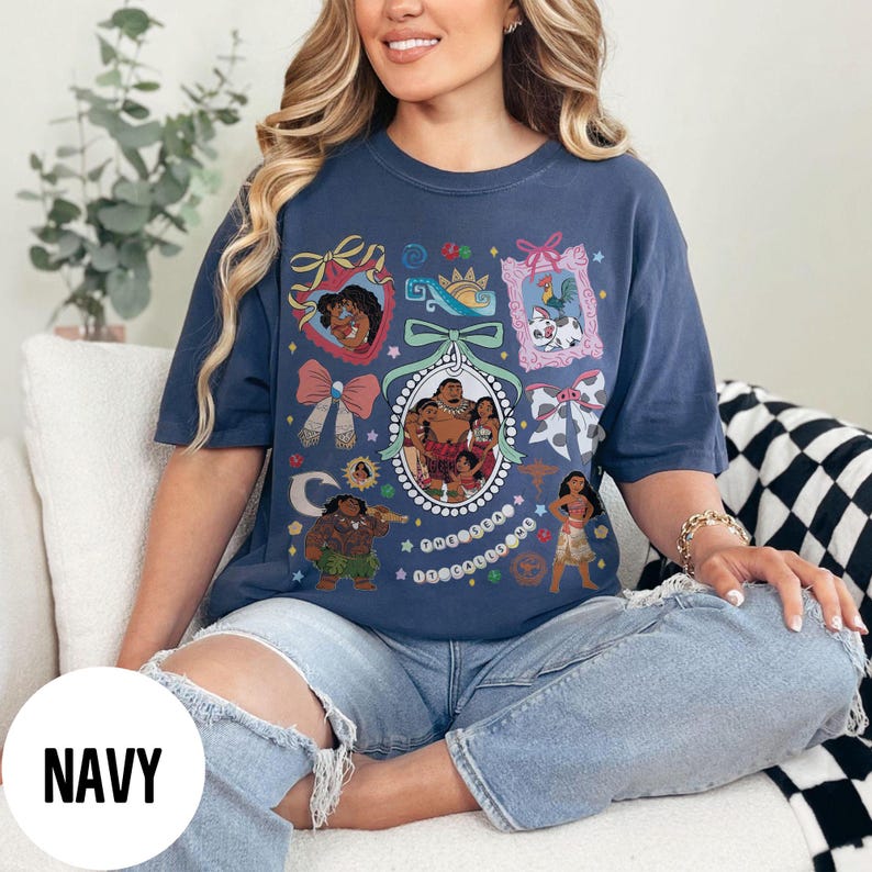 Pu&ograve; includere: T-shirt blu navy con un design grafico colorato con personaggi dei cartoni animati. Il design include una cornice ovale centrale con un ritratto di famiglia e altre immagini incorniciate. La parola "NAVY" &egrave; stampata su un cerchio bianco.