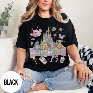 May include: Black t-shirt with a colorful Disneyworld graphic. The design features a castle, Winnie the Pooh characters, and the word "Disneyworld" in pastel colors. The shirt is a classic crew neck.