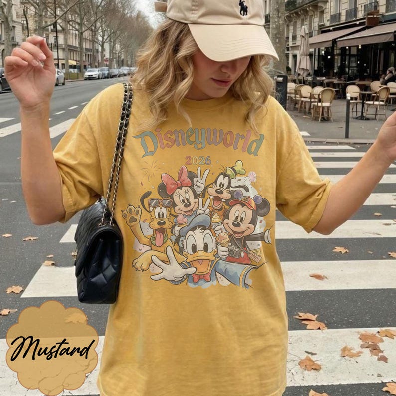 Pu&ograve; includere: T-shirt giallo senape con grafica Disneyworld 2026 con Topolino, Minnie, Paperino, Pippo e Pluto. La maglietta ha girocollo e maniche corte. La parola "Mustard" &egrave; scritta in corsivo.