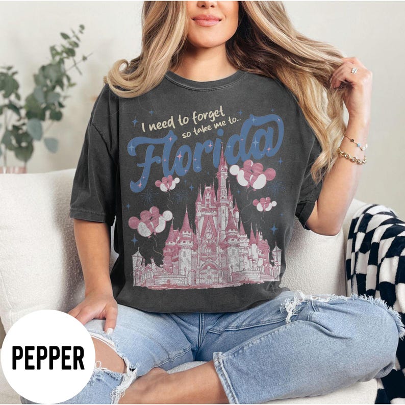 May include: Dark gray t-shirt with the text "I need to forget so take me to... Florida" in blue and pink. The shirt features a pink and white castle design with balloons. The word "PEPPER" is in a white box at the bottom.