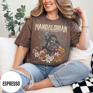 Puede incluir: Camiseta color espresso con un gr&aacute;fico de The Mandalorian y Grogu rodeados de flores y mariposas. El texto "MANDALORIAN - THIS IS THE WAY" est&aacute; impreso en la parte superior. La camiseta es de corte holgado.