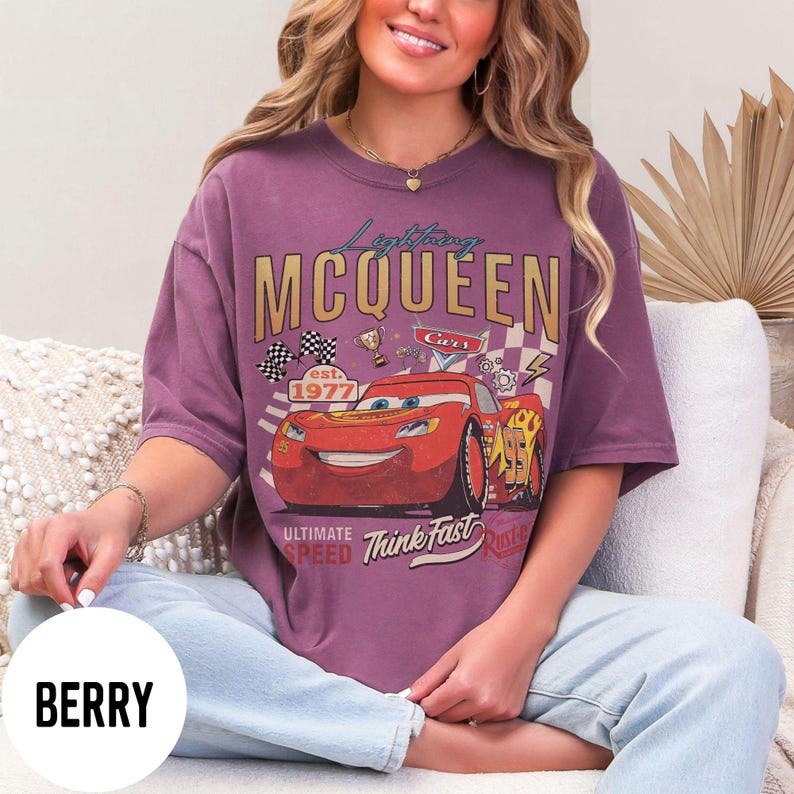 Op de afbeelding: Bessenkleurig T-shirt met een Lightning McQueen-afbeelding uit de film Cars. Het ontwerp bevat de tekst "Lightning McQueen" en "Cars", racevlaggen en het jaar "1977". Het shirt heeft een vintage, distressed look.