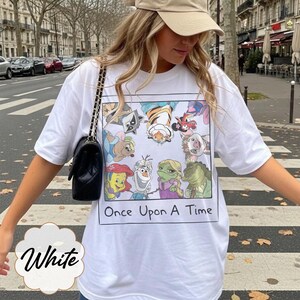 May include: White t-shirt featuring a colorful cartoon graphic with the text "Once Upon A Time." The graphic includes various animated characters. The shirt is a casual style.