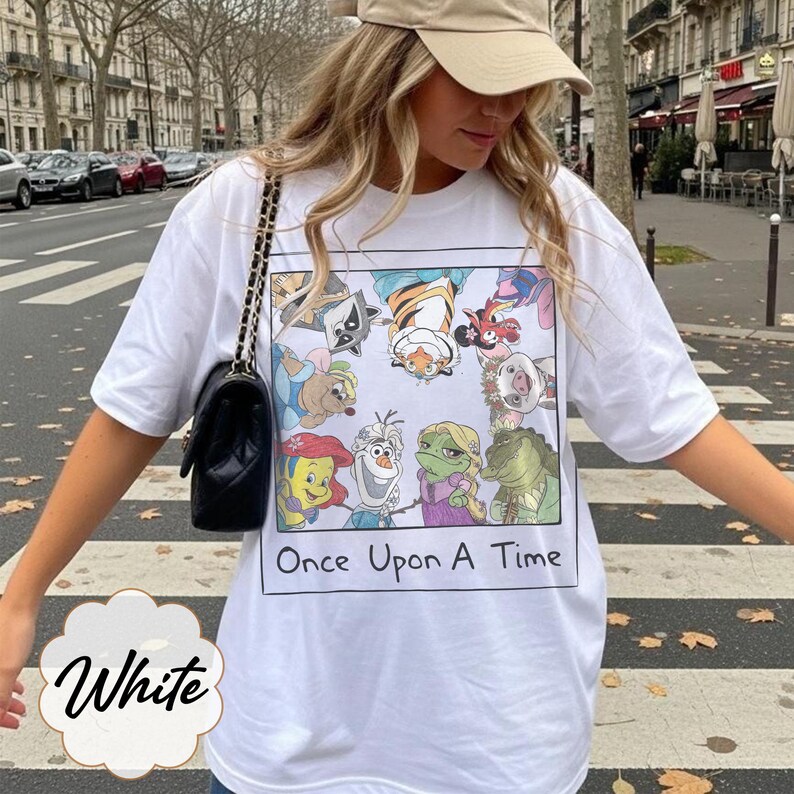 May include: White t-shirt featuring a colorful cartoon graphic with the text "Once Upon A Time." The graphic includes various animated characters. The shirt is a casual style.