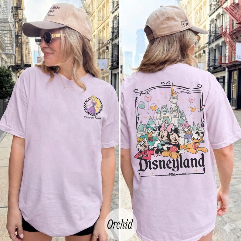 Pu&ograve; includere: T-shirt color orchidea con grafica frontale di una principessa in un cerchio a scacchi e la scritta "Custom Name". Il retro della maglietta mostra una grafica di Disneyland con personaggi dei cartoni animati e la scritta "Disneyland 1955".
