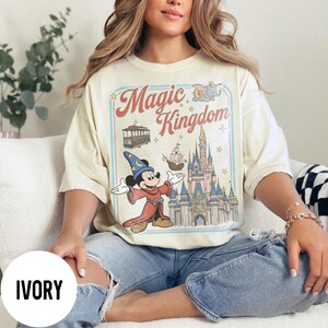 May include: Ivory-coloured t-shirt with a vintage graphic of Mickey Mouse as a wizard, in front of Cinderella's castle, and the words "Magic Kingdom". The shirt has a relaxed fit.