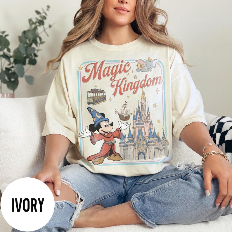May include: Ivory-coloured t-shirt with a vintage graphic of Mickey Mouse as a wizard, in front of Cinderella's castle, and the words "Magic Kingdom". The shirt has a relaxed fit.