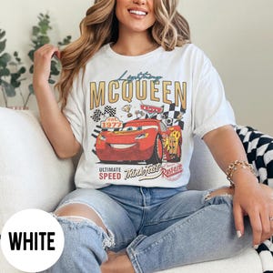 Op de afbeelding: Wit T-shirt met een Lightning McQueen-afbeelding uit de film Cars. De afbeelding bevat de tekst "Lightning McQueen", "Cars" en "Ultimate Speed Think Fast Rusteze". Het ontwerp toont een rode raceauto, geblokte vlaggen en trofee details.