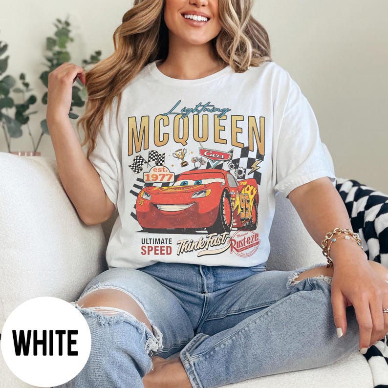 Op de afbeelding: Wit T-shirt met een Lightning McQueen-afbeelding uit de film Cars. De afbeelding bevat de tekst "Lightning McQueen", "Cars" en "Ultimate Speed Think Fast Rusteze". Het ontwerp toont een rode raceauto, geblokte vlaggen en trofee details.