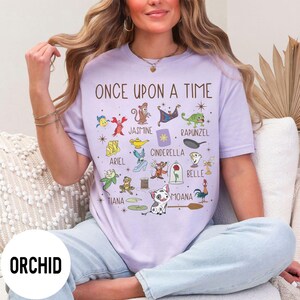 May include: A lilac t-shirt with the words "ONCE UPON A TIME" and cartoon character illustrations. The shirt features characters like Ariel, Jasmine, Cinderella, and Belle. The word "ORCHID" is printed on the bottom left.