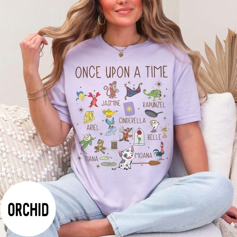 May include: A lilac t-shirt with the words "ONCE UPON A TIME" and cartoon character illustrations. The shirt features characters like Ariel, Jasmine, Cinderella, and Belle. The word "ORCHID" is printed on the bottom left.
