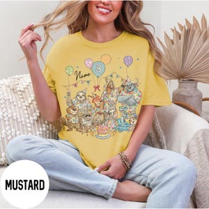 以下が含まれることがあります： マスタードイエローのTシャツ。誕生日を祝う擬人化された動物たちのカラフルなイラストが特徴です。デザインには風船、ケーキ、数字の3が含まれています。「Name」の文字も表示されています。カジュアルなスタイルです。