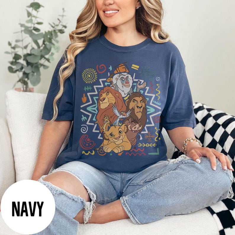 Puede incluir: Camiseta azul marino con un gr&aacute;fico colorido de personajes de una popular pel&iacute;cula de animaci&oacute;n. El dise&ntilde;o incluye leones, un suricato, un jabal&iacute; y un mono, rodeados de formas geom&eacute;tricas. La palabra "NAVY" est&aacute; impresa en un c&iacute;rculo blanco.