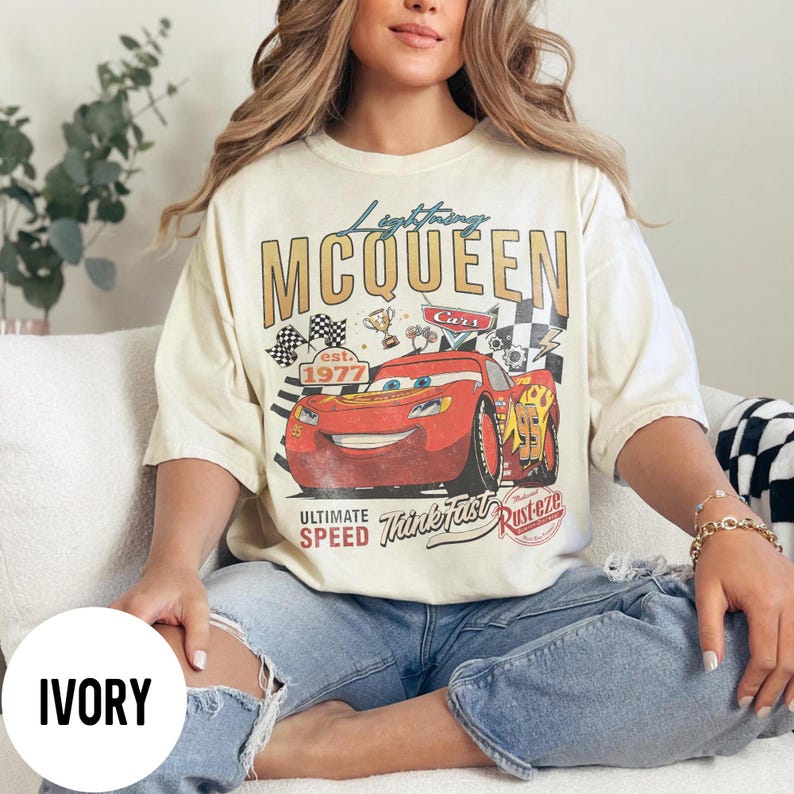 Op de afbeelding: Ivoor kleurig Lightning McQueen grafisch t-shirt. Het ontwerp toont het personage Lightning McQueen uit de Cars-film, samen met de tekst "Lightning McQueen" en "est. 1977". Het shirt heeft een vintage, distressed look.