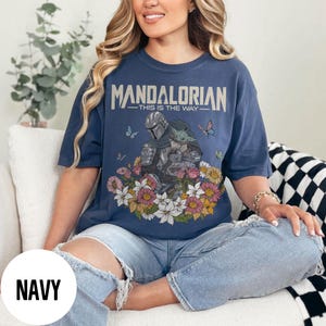 Puede incluir: Camiseta azul marino con un dise&ntilde;o de The Mandalorian y Grogu rodeados de flores y mariposas. El texto "MANDALORIAN - THIS IS THE WAY" est&aacute; impreso en la parte superior. La camiseta es de corte holgado.