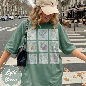 May include: Light green t-shirt with a grid of cartoon sketches and the text "Light Green". The sketches are of various characters. The shirt is a light green color.