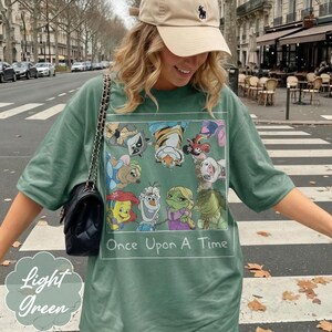 May include: Light green t-shirt with a rectangular graphic featuring cartoon characters and the text "Once Upon A Time." The shirt also has the words "Light Green" in a decorative font.
