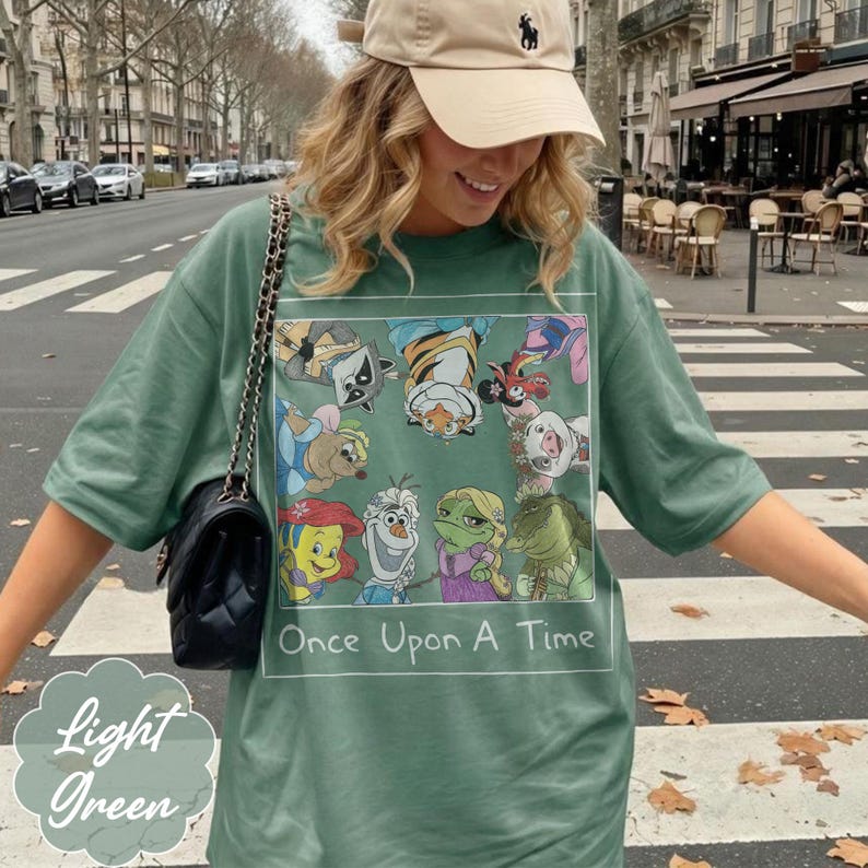 May include: Light green t-shirt with a rectangular graphic featuring cartoon characters and the text "Once Upon A Time." The shirt also has the words "Light Green" in a decorative font.