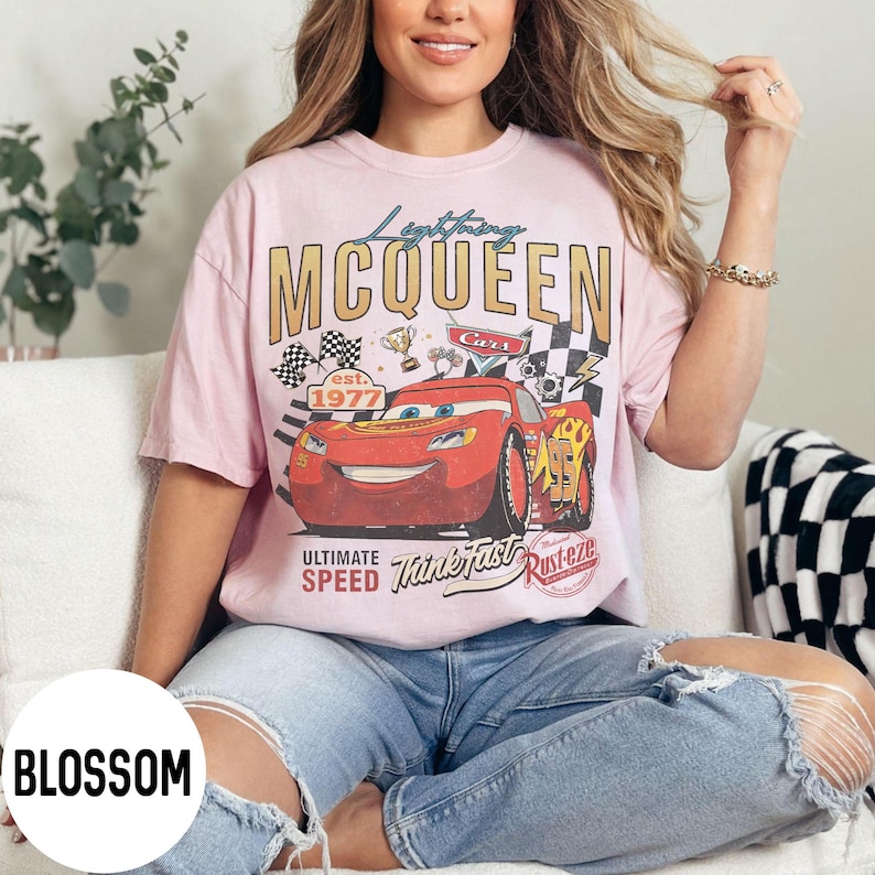 Op de afbeelding: Zachtroze t-shirt met een Lightning McQueen-afbeelding. Het ontwerp toont een rode raceauto, geblokte vlaggen en de tekst "Lightning McQueen" en "Ultimate Speed". De shirt heeft ook "est. 1977".
