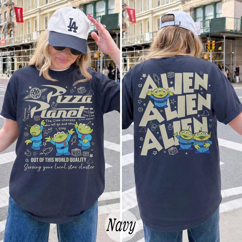 K&ouml;nnte beinhalten: Marineblaues T-Shirt mit einem Pizza Planet-Motiv auf der Vorderseite und Alien-Charakteren auf der R&uuml;ckseite. Das Frontdesign enth&auml;lt den Text "Pizza Planet" und Cartoon-Aliens. Das R&uuml;ckendesign zeigt das Wort "Alien" dreimal wiederholt.