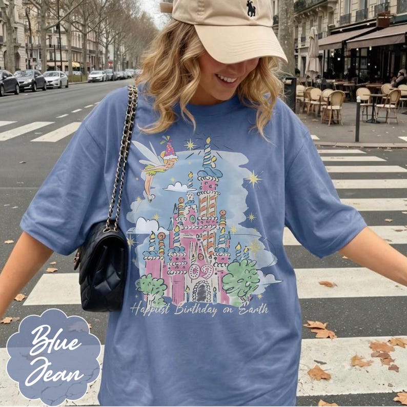 Puede incluir: Camiseta azul vaquero con un gr&aacute;fico colorido de un castillo, un hada y el texto "Happiest Birthday on Earth". La camiseta tiene mangas cortas y un corte holgado. Un peque&ntilde;o texto "Blue Jean" est&aacute; en la esquina inferior izquierda.