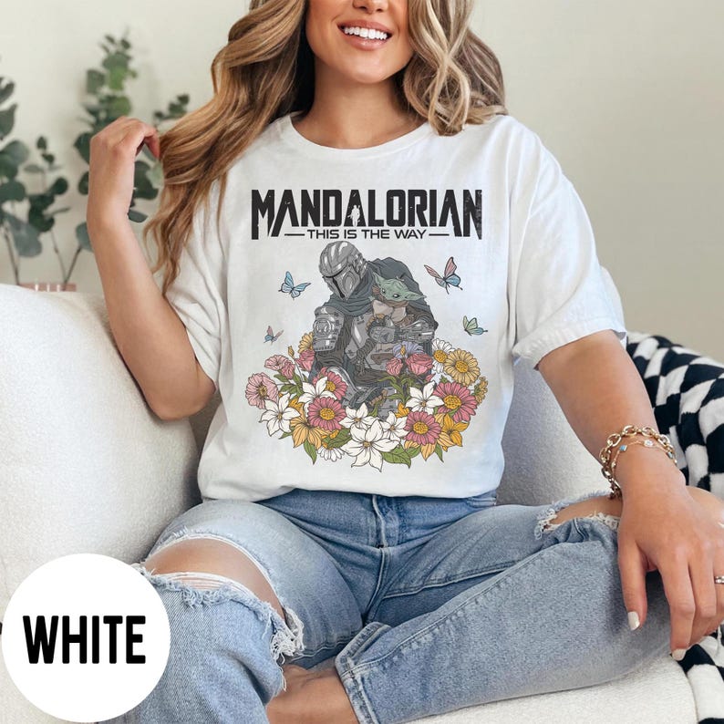 Puede incluir: Camiseta blanca con la frase "MANDALORIAN - THIS IS THE WAY" y un gr&aacute;fico del Mandaloriano y Grogu, rodeados de flores y mariposas. La camiseta tiene un corte holgado.